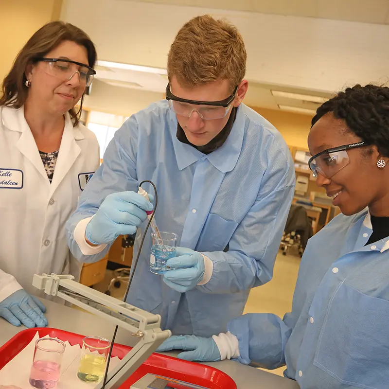 Two female researchers watch male researcher work with test tube in lab