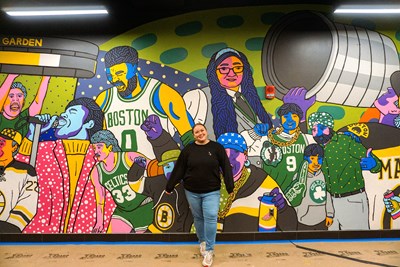 A woman paints a mural that has people painted in bright colors.