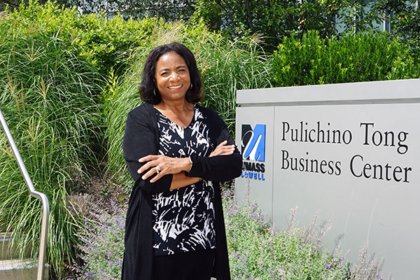 A woman poses for a photo with her arms folded while standing in front of a business school sign