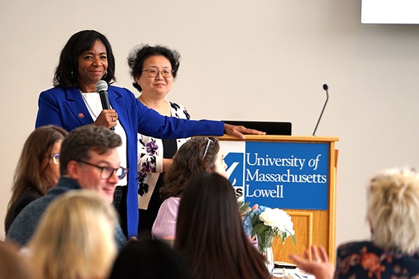 A woman holds a microphone while standing at a podium and listening to a woman talk