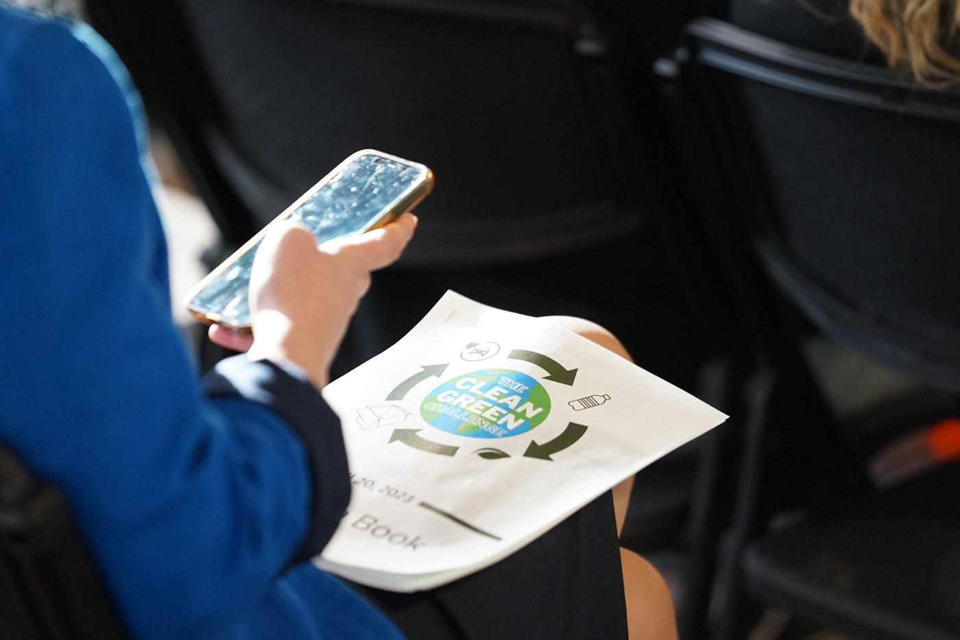 Person looking at phone in hand with flyer on lap
