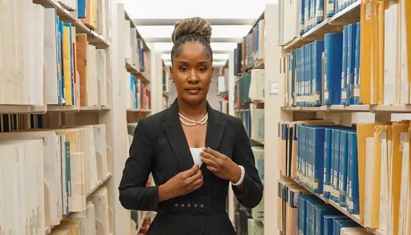 Erlande Fevrier poses between book stacks in a library.