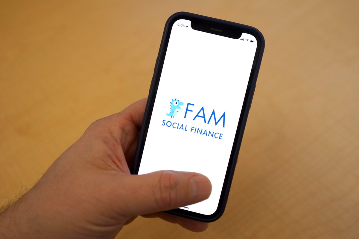 A hand holds a phone with the FAM social finance app open on the screen.