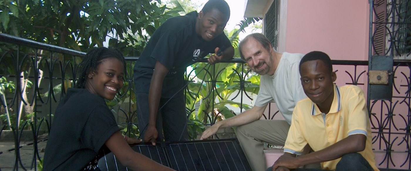 UMass Lowell Professor, Bob Giles poses with three Haitian teens while holding solar panels.