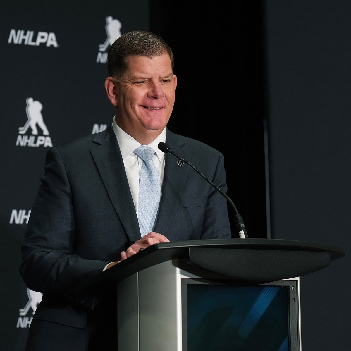 Marty Walsh standing at a podium with a background with letters NHLPA and a silhouette of a hockey player.