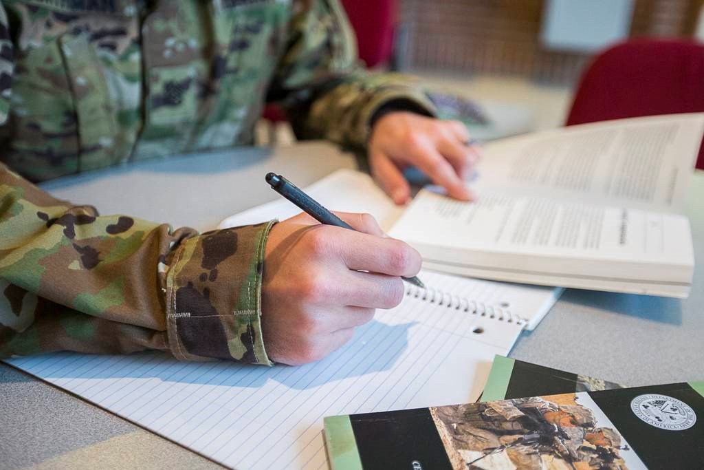 Stock image of soldier taking notes while holding a book sitting at a table.