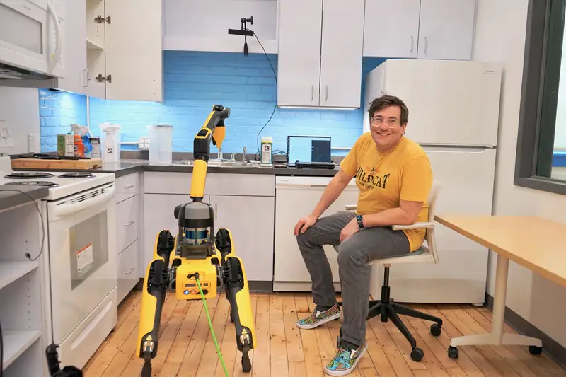 Russ Perkins poses with a robot in a kitchen.