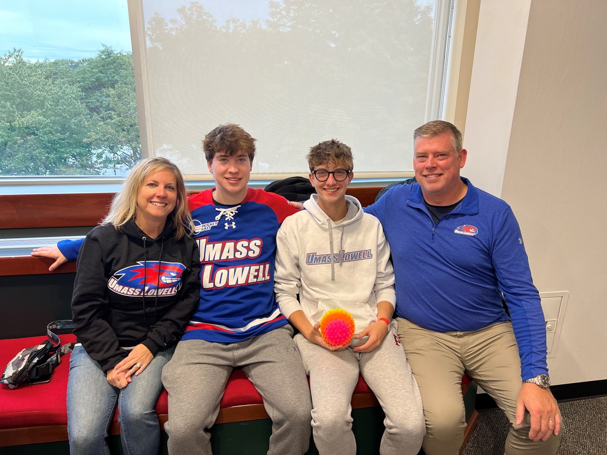 Mother, 2 sons and a Father all dressed in UMass Lowell gear sitting on a couch.