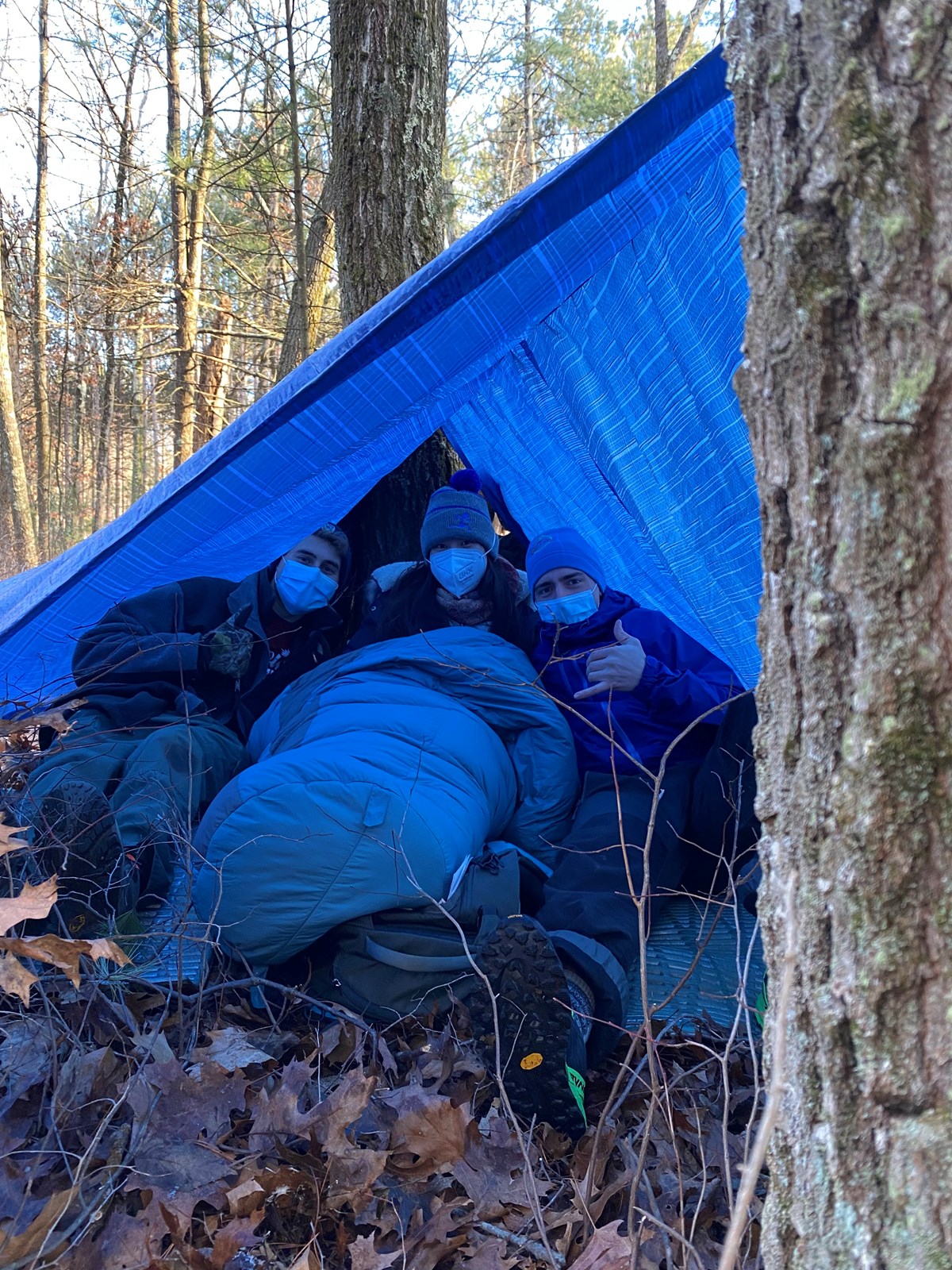 Three people sit outside on the leafy ground under a tarp in a practice medical scenario