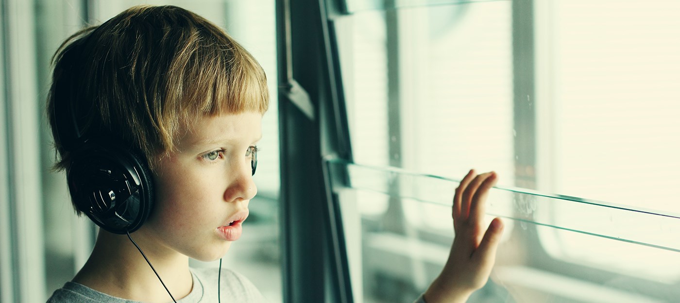 Young boy wearing headphones and staring out the window at the airport.