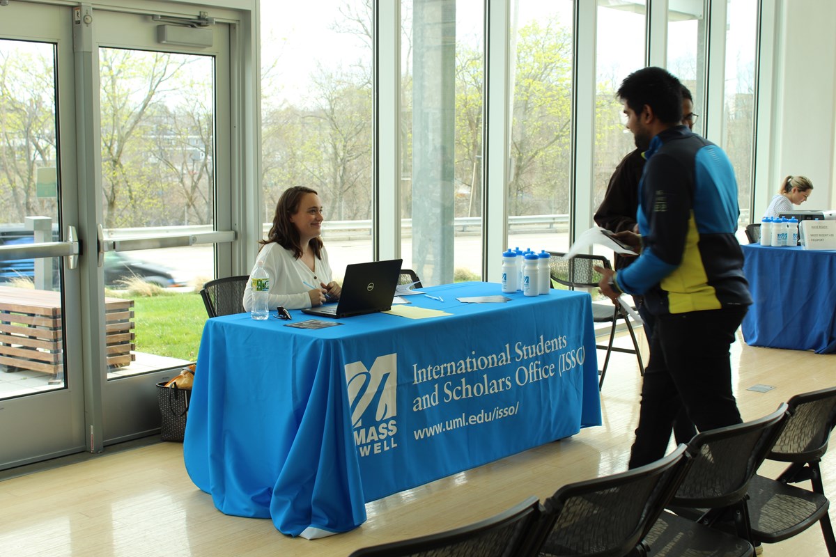 Staff at table talking to students. Table cover says: UMass Lowell, International Students & Scholars Office (ISSO) & www.uml.edu/isso/.