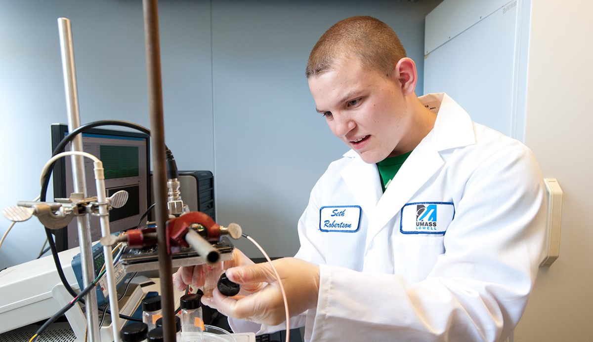 A male UMass Lowell student wearing a lab coat and working in a Civil & Environmental Engineering lab.
