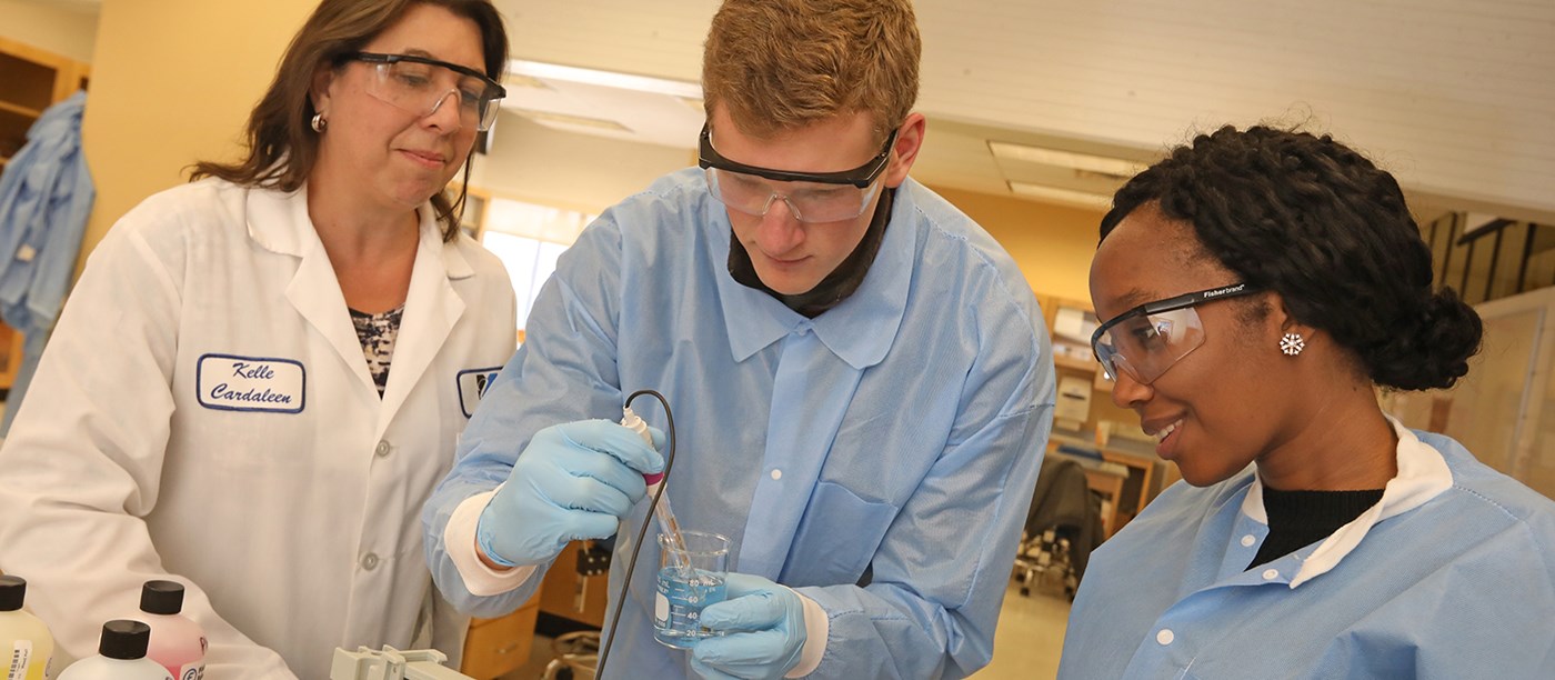 Two students conduct experiment in lab as female professor looks on