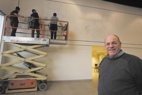 Salesman James Dabilis of Lowell, right, enjoys watching the mural take shape in the Drum Hill Ford showroom thanks to the talent and skills of Carlos Pujols, Josh Rondeau and Courtney LeMay. 