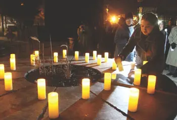 Cari Renn of Lowell, who was a friend of Sandy Hook Elementary School teacher and victim Lauren Rousseau, places the name of a victim under an electric candle during a vigil at UMass Lowell Thursday night.