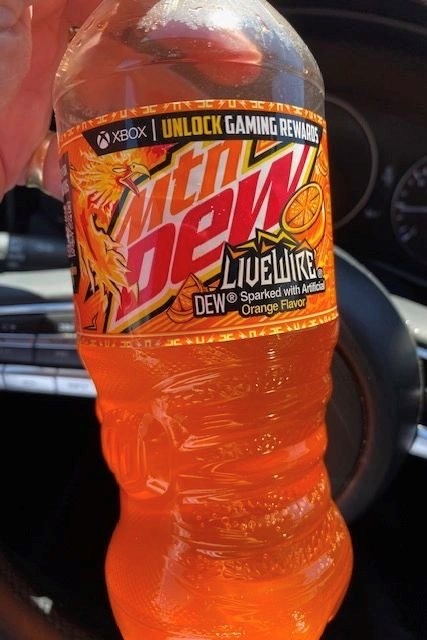 A person takes a photo of an orange soft drink in their car.