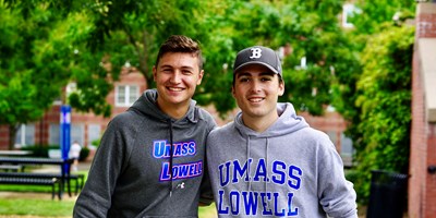 Two students wearing UMass Lowell sweatshirts with their arms around each other on East Campus