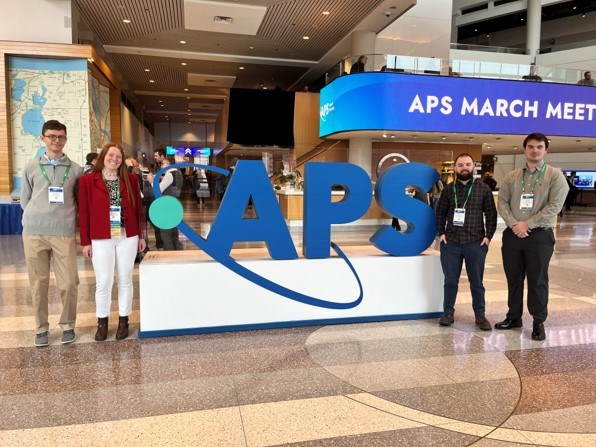Students standing around the American Physical Society sign at the conference.