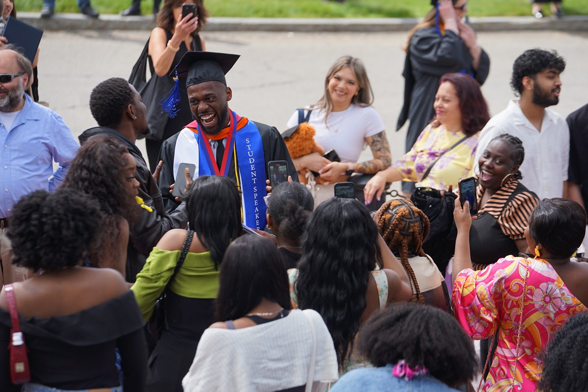 A person in cap and gown is surrounded by people outside.