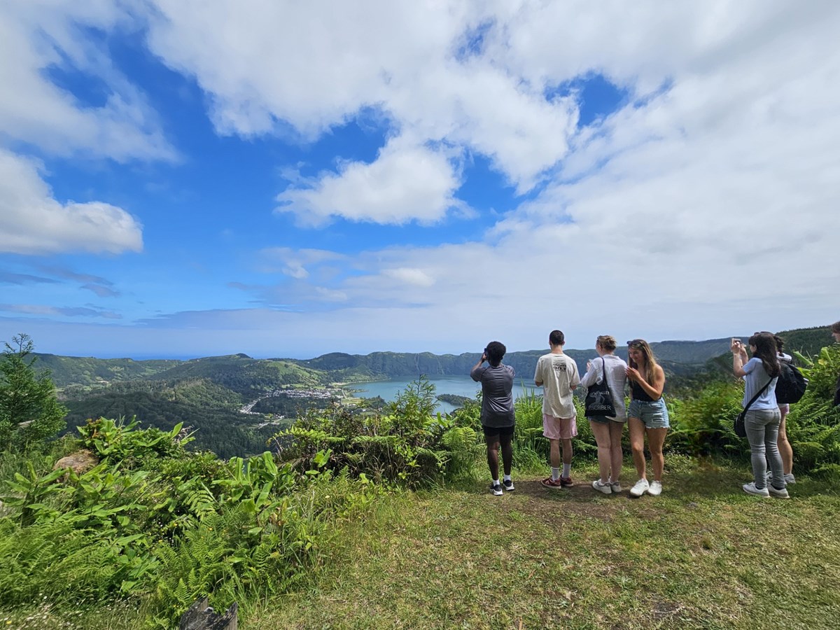 Students on a cliff in the Azores viewing a lake and the sky.