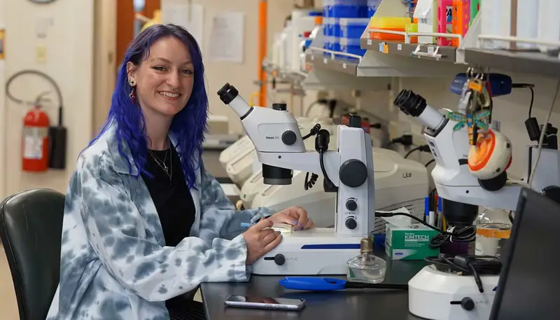 CeCe Allen poses with a microscope in a UMass Lowell lab.