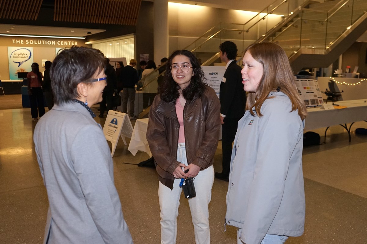 Three people chat with each other while standing in the lobby of a building.