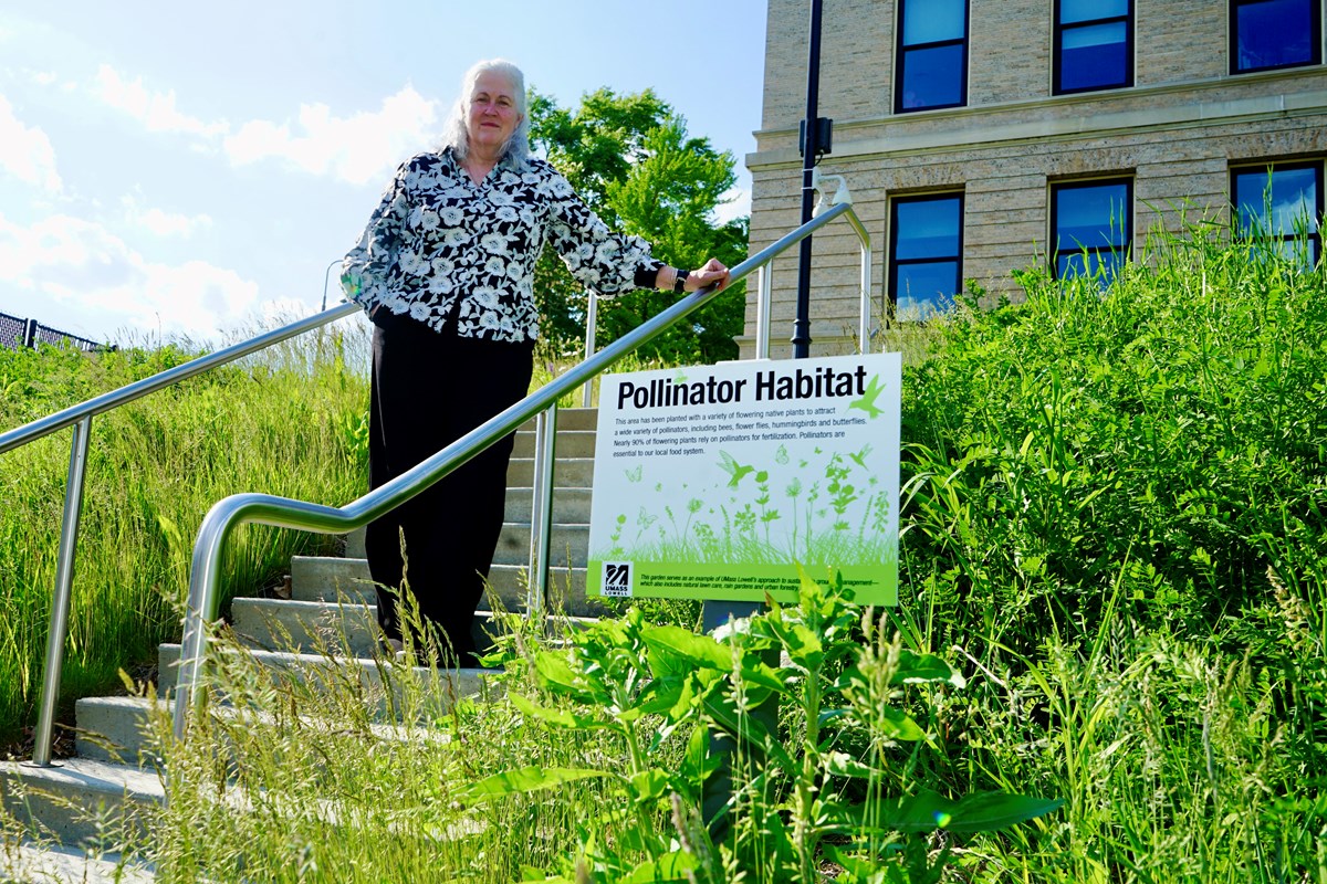 A person stands on a stairway outside next to a pollinator garden.
