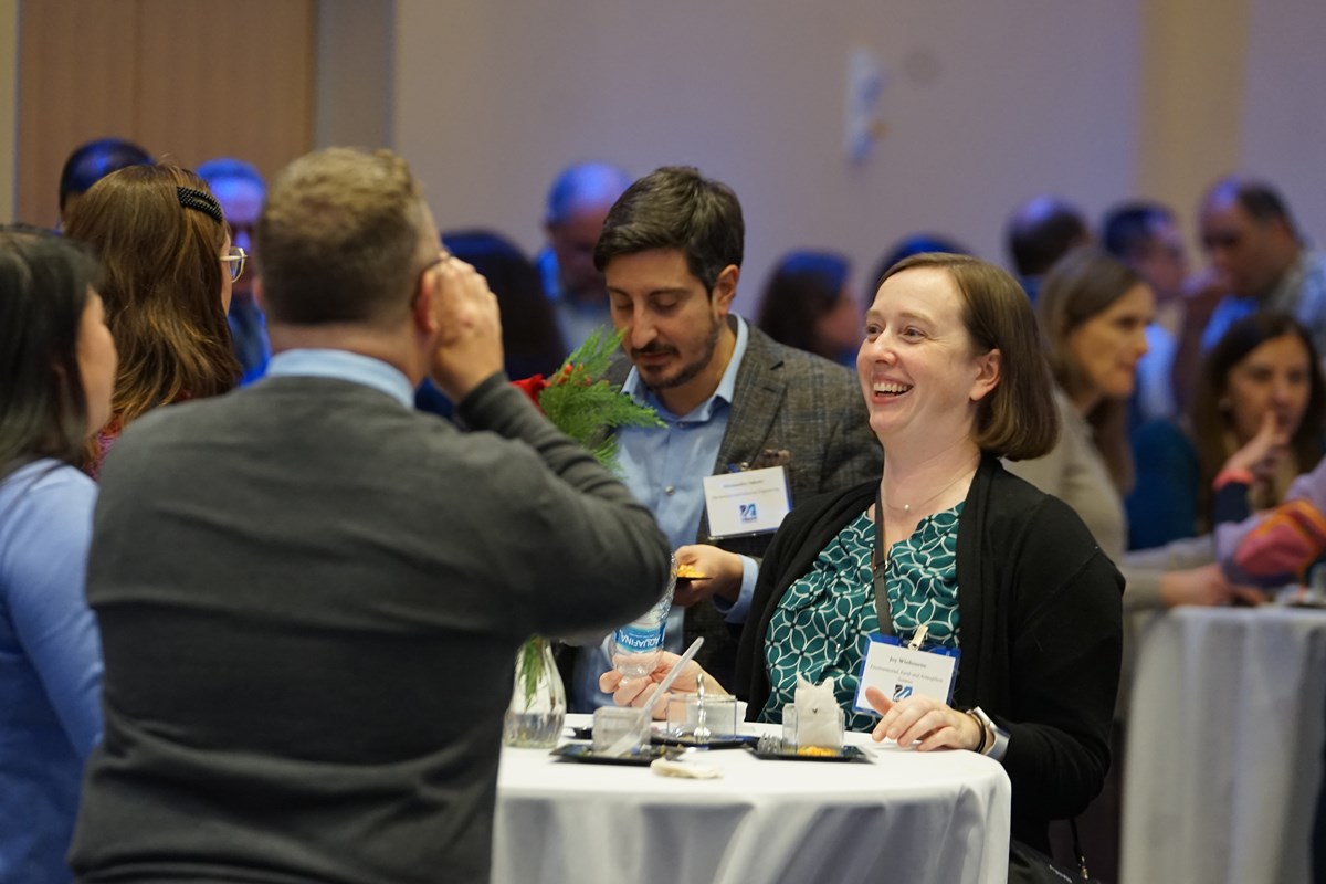 Faculty member smiling and networking with three others at a cocktail table.