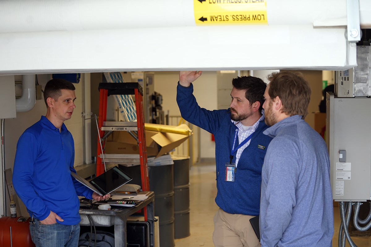 Three people talk to each other while standing below an overhang.