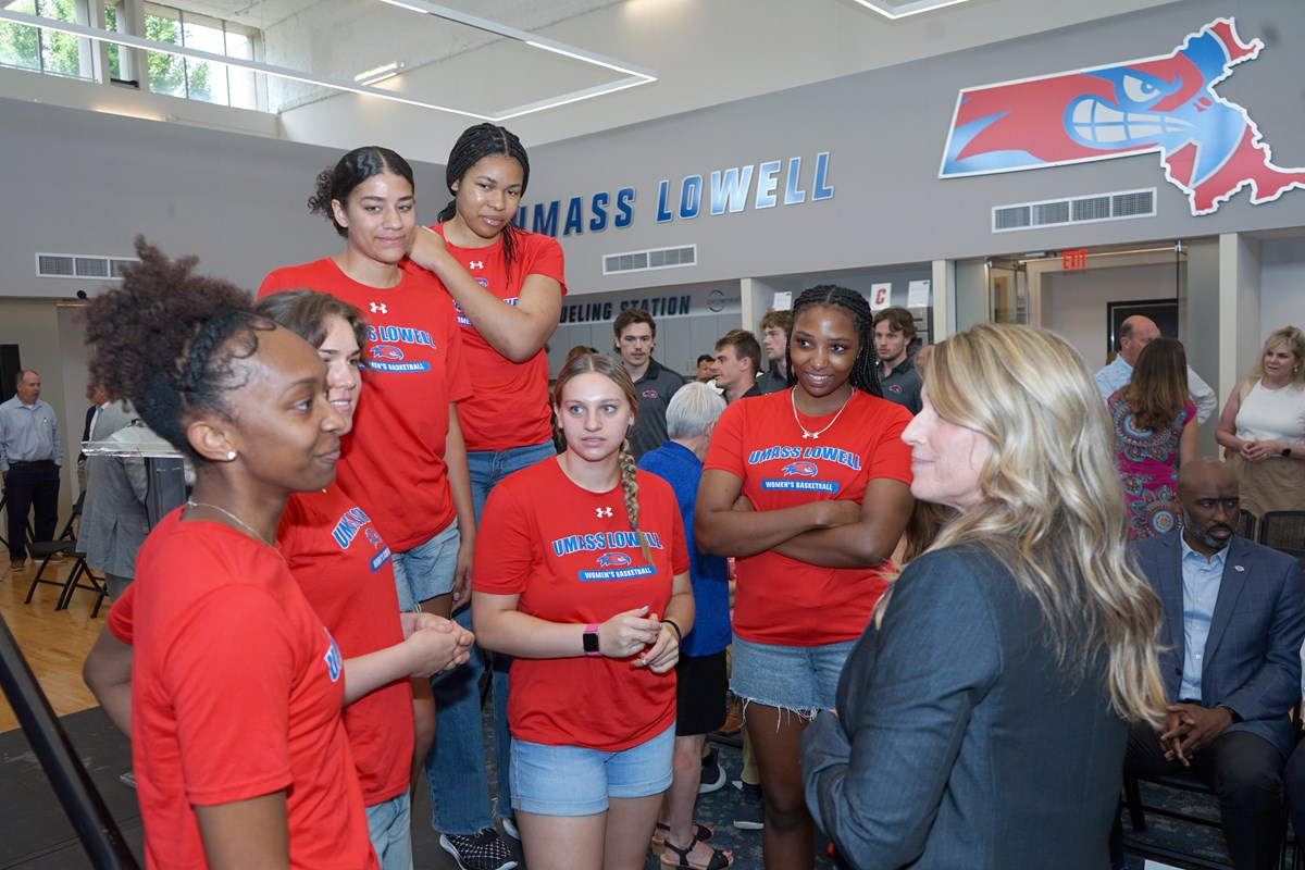 A woman in a blazer talks to six women's college basketball players wearing red T-shirts.