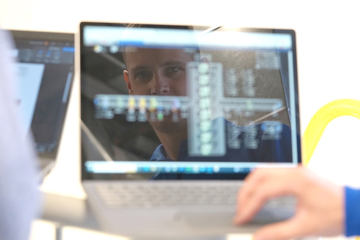 A person's face is reflected in a laptop screen while a hand is on the keyboard.