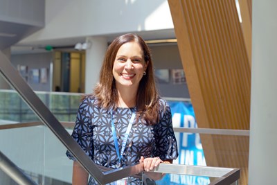 A person with brown hair wearing a blue dress poses for a photo on a stairway landing.