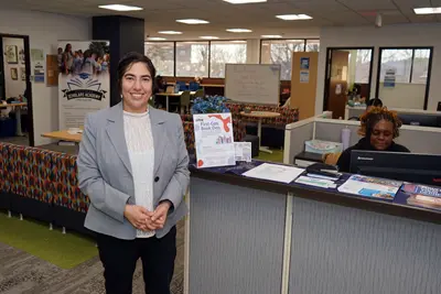 A woman in a gray blazer poses for a photo while standing near the reception desk in a college office.