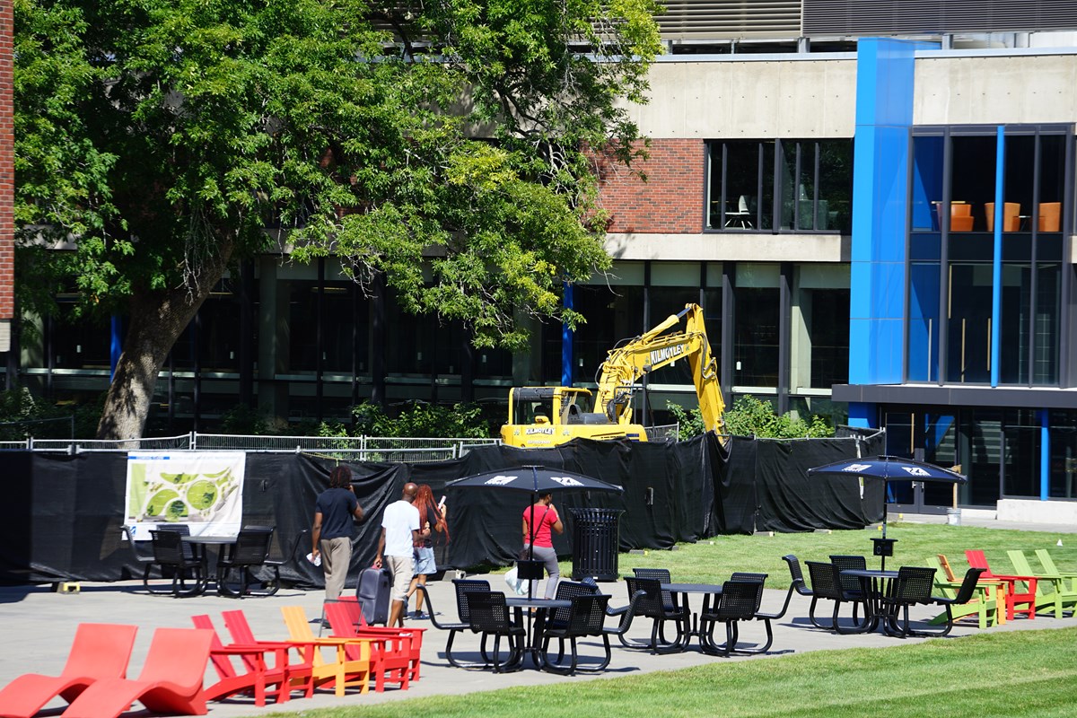 Four people walk past construction fencing on a campus quad.