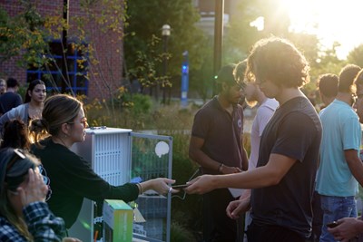 Four young people sit at a round table in a college dining hall and read cards to one another.