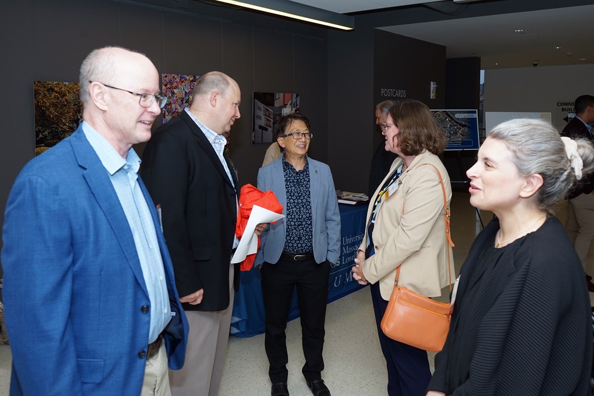 Five people are engaged in conversations while standing in a foyer of a building.