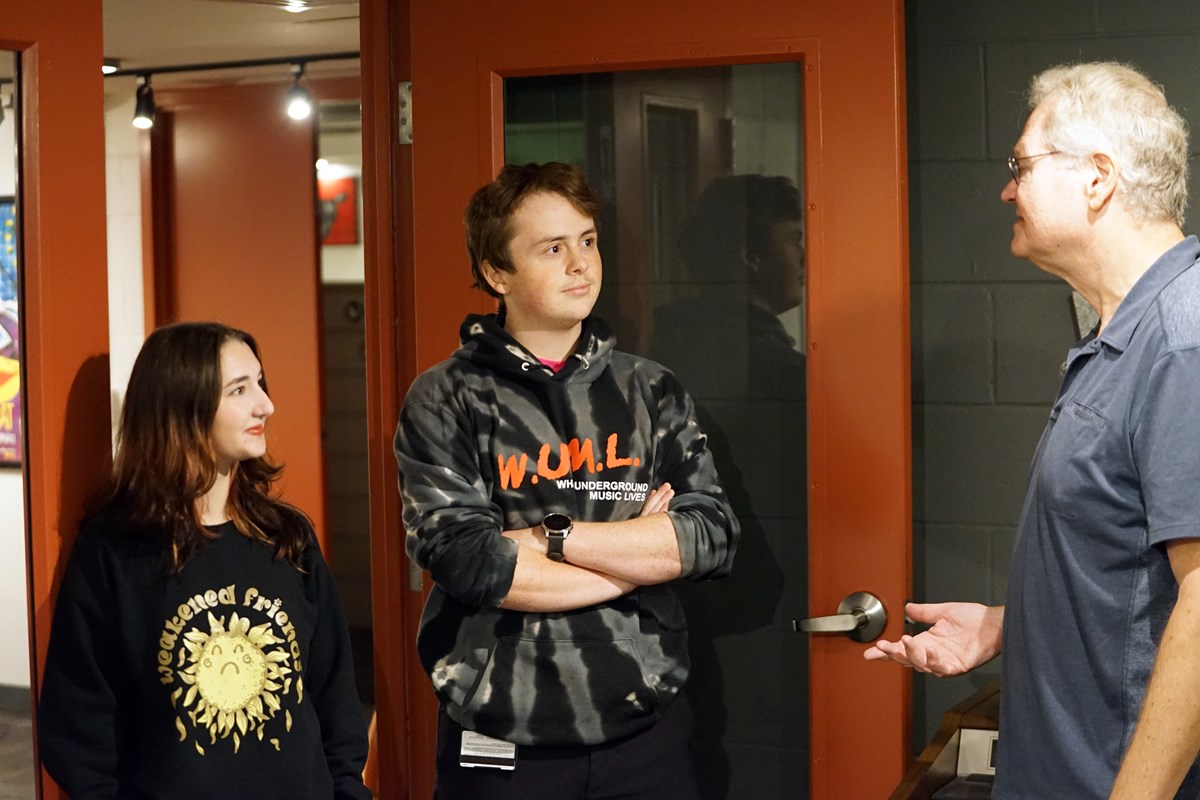 Two college students talk to a man in the doorway of a college radio station.