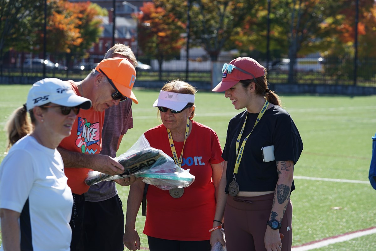 Two women and a man look at pickleball paddles that are wrapped in plastic.