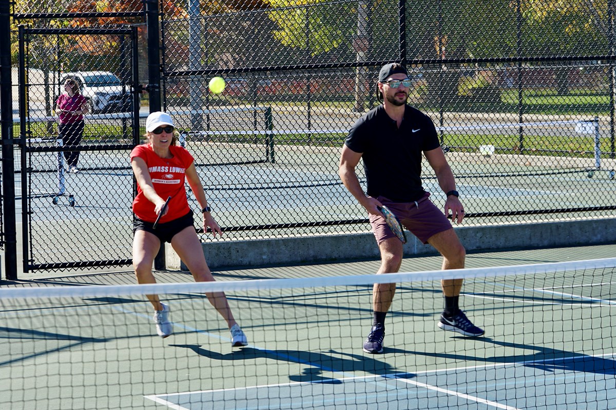 A woman in white hat and red T-shirt hits a shot while her pickleball partner looks ahead.