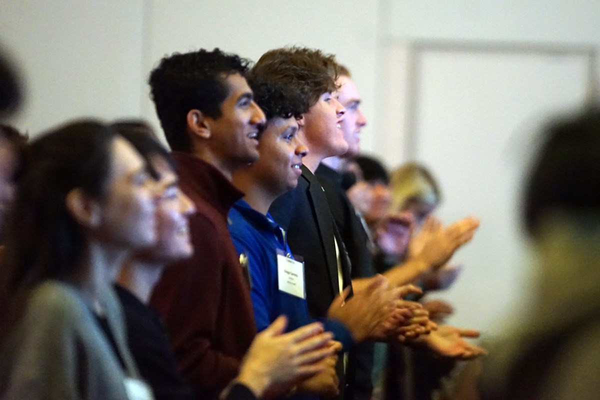 A row of a half dozen young people stand and applaud while smiling.