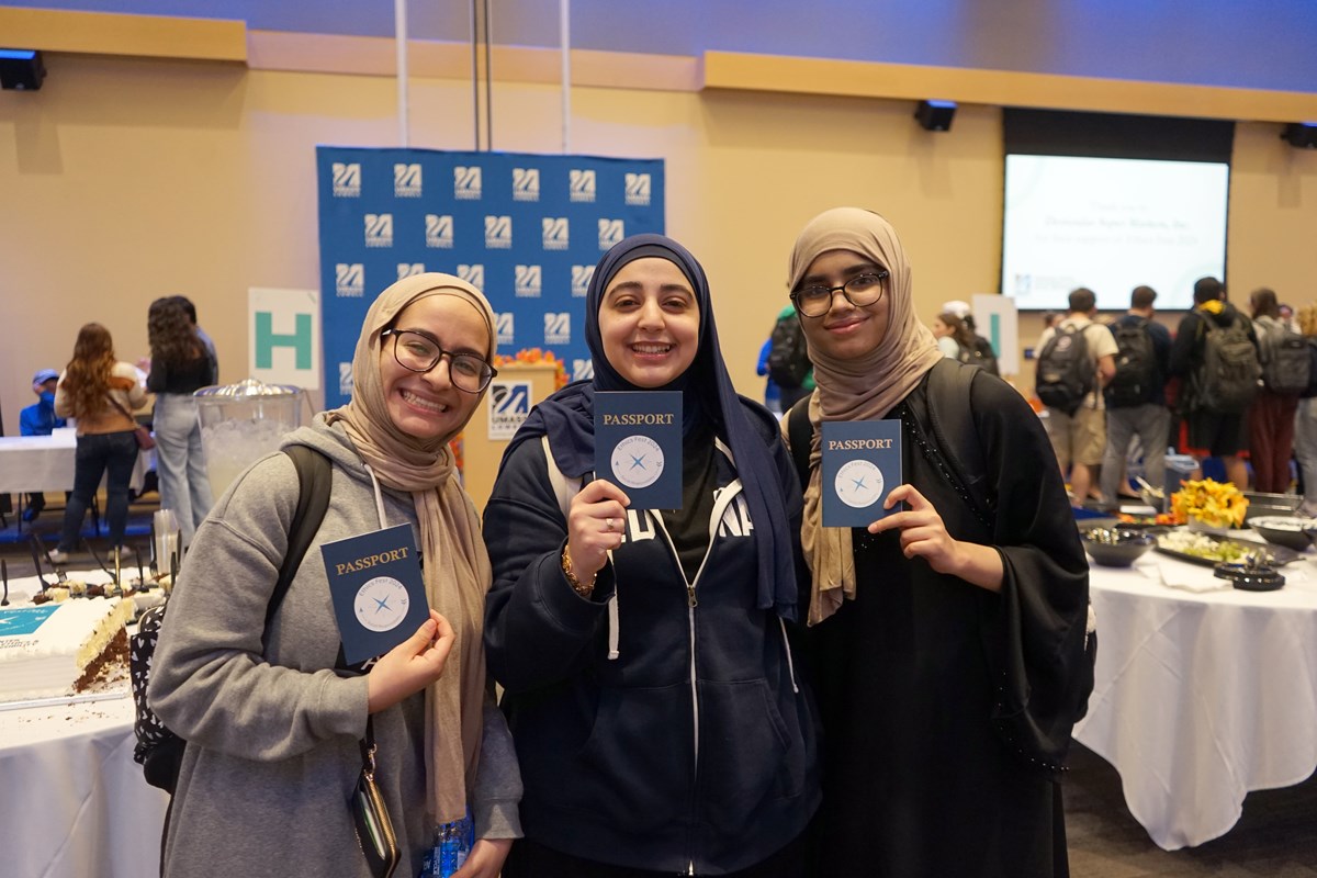 Three young women pose for a photo while holding Ethics Fest passports in a large room.