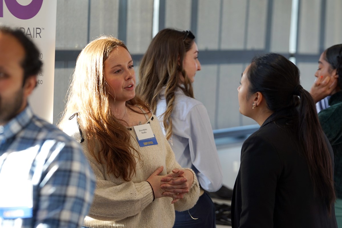 A woman with long hair folds her hands while talking to a student with dark hair.