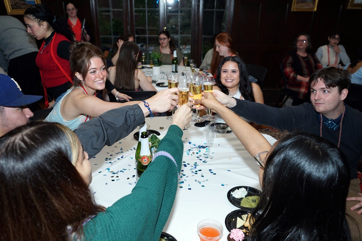 Six people make a toast with champagne glasses while sitting at a table.