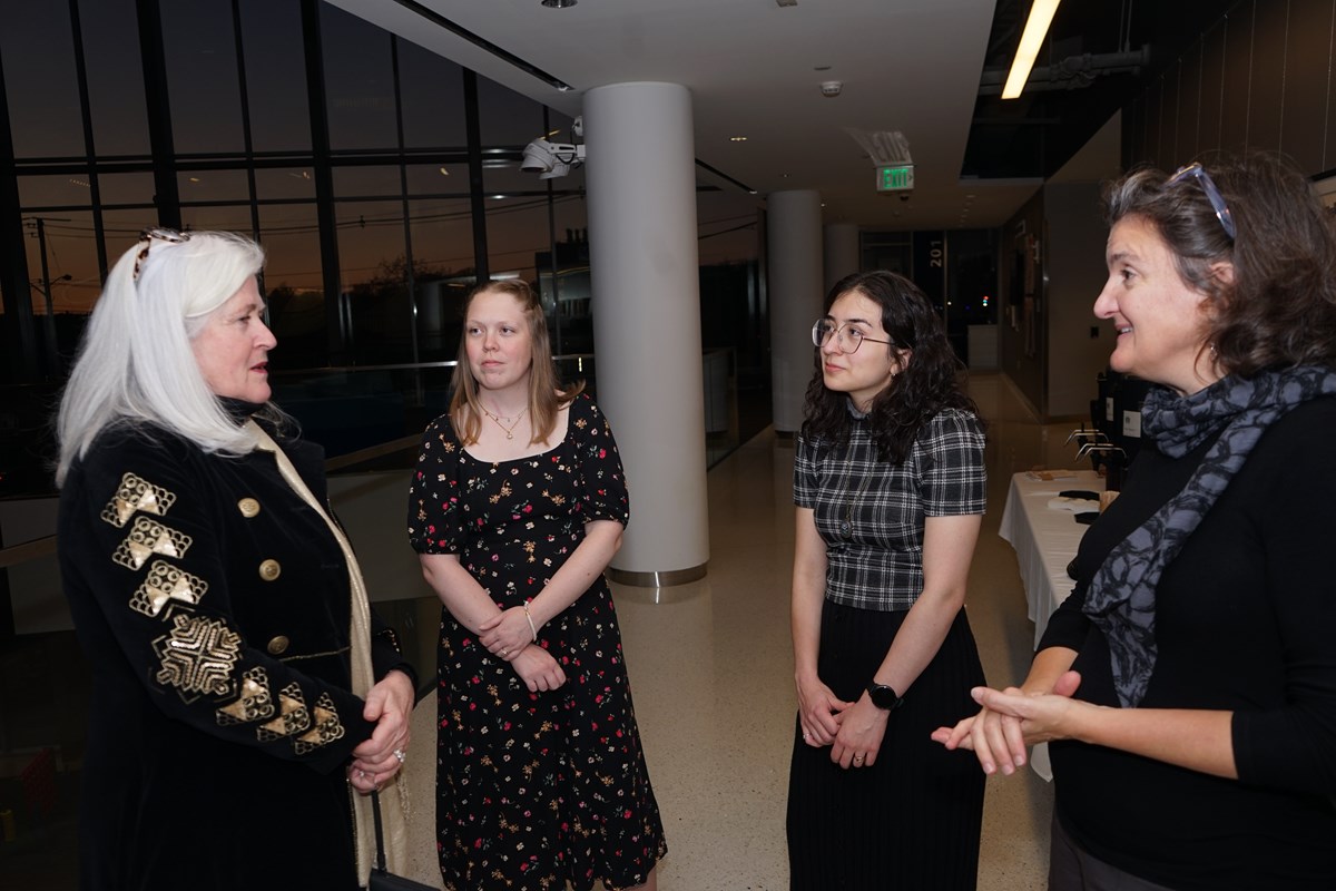 Four people stand in a semicircle and talk on the landing of a building.