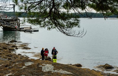 A group of four individuals stand on the banks of the Damariscotta River with a getty in the background