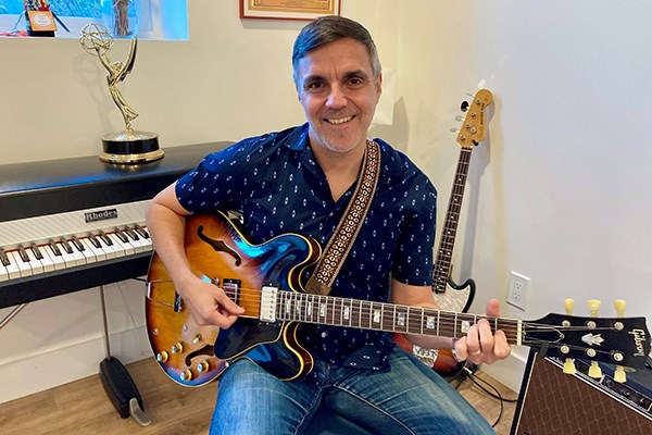 Eric Casimiro plays an electric guitar with an electric keyboard and an Emmy statuette behind him