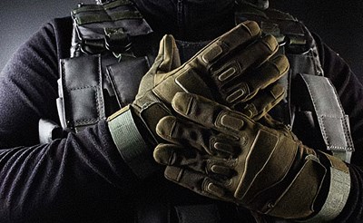 Soldier with their gloves in full view. The gloves are tan against a dark backdrop and a dark uniform.
