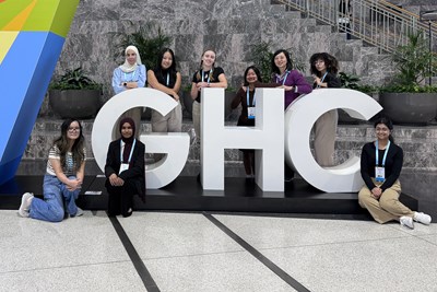 Eight students and a professor stand beside a GHC sign.