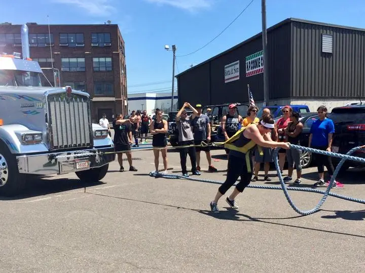 A woman pulls a tractor trail truck down a street while people watch.