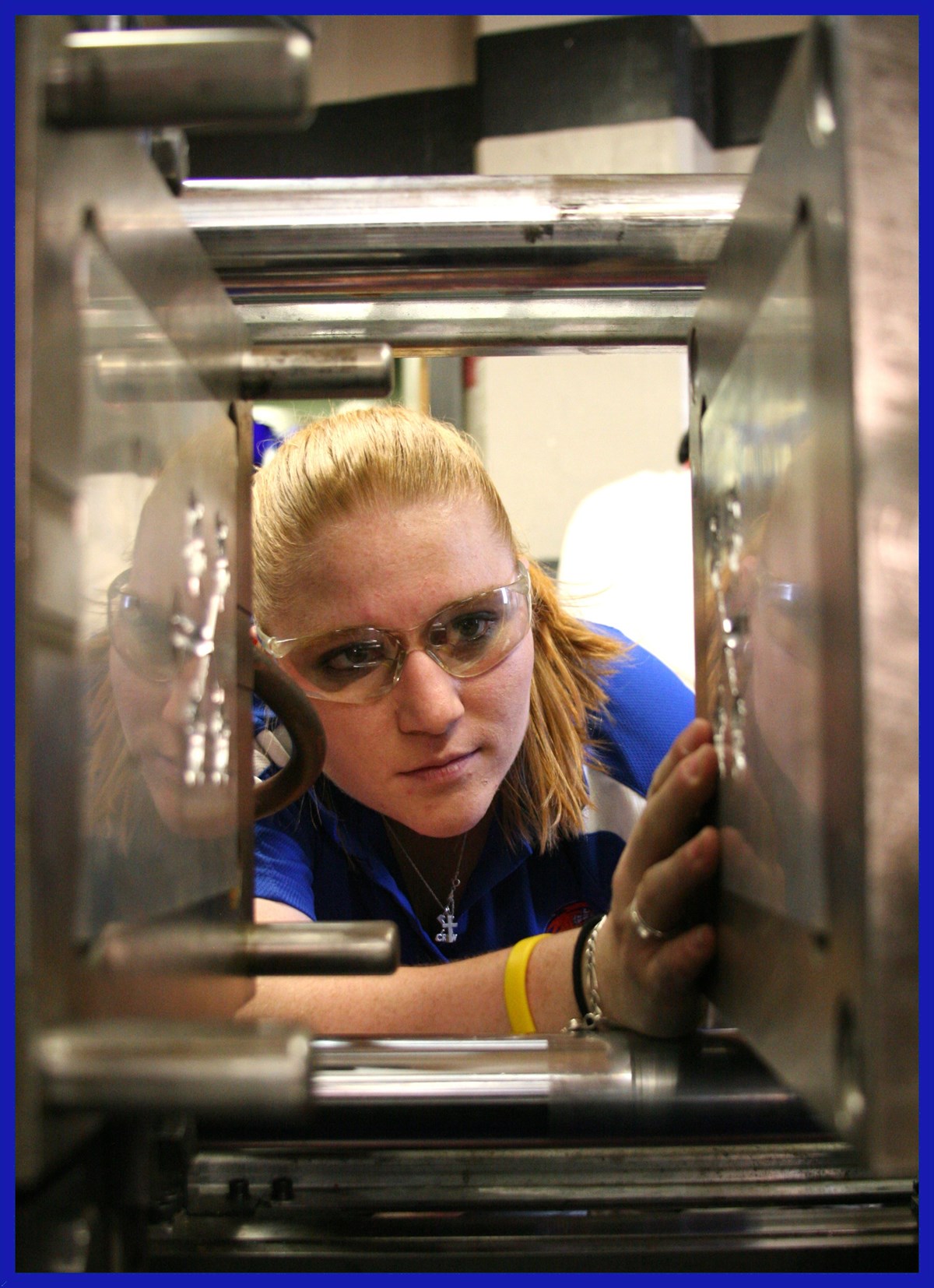 A student with safety goggles looks through machinery in a plastics engineering lab.